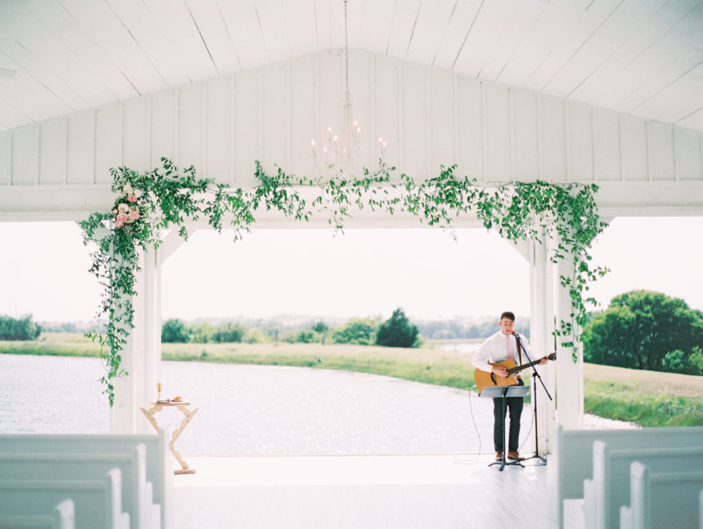 Musicista con chitarra alla cerimonia di nozze, sedie bianche e decorazioni floreali verdi